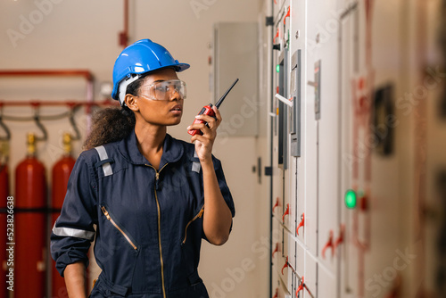 Professional engineer black women working with tablet at warehouse factory. Engineer Worker Wearing Safety Uniform and Hard Hat. Female  checking at electrical cabinet control.