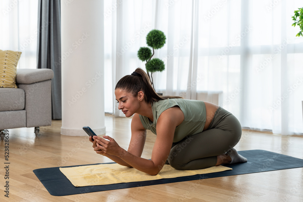 Fototapeta premium Happy attractive young business woman in active sport wear sitting on stretching muscles at her apartment after or before the work, training yoga class. Home workout as stress and pain relief.