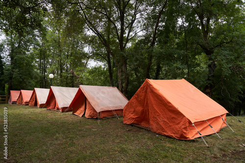 Side view of a group of orange tents by the river, newly pitched to receive the children of the camp.