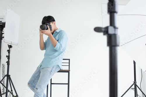 An Asian male photographer took a photo in the studio and sit on the chair With studio lights as a backdrop and copy space.
