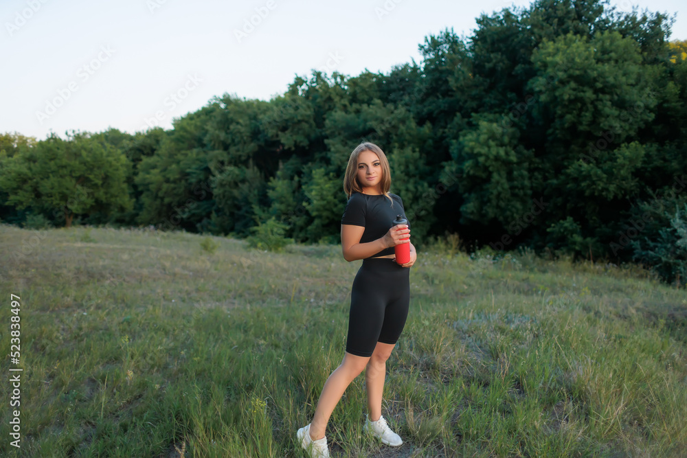 blonde sportswoman in the park posing with a red bottle of water at sunset blonde sportswoman in the park posing with a red bottle of water at sunset