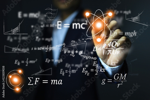 The man's hand points to the atomic equation of relativity by Albert Einstein. E equals m multiplied by c squared. In the concept of a physics equation ring.