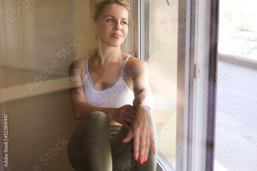 Beautiful elegant woman sitting on window sill and smiling. Young blond girl thoughtful and looking outside Free Download Beautiful elegant woman sitting on window sill and smiling. Young blond girl thoughtful and looking outside - GFXLoad