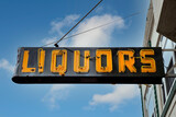 Orange on black LIQUORS sign attached to building with blue sky.