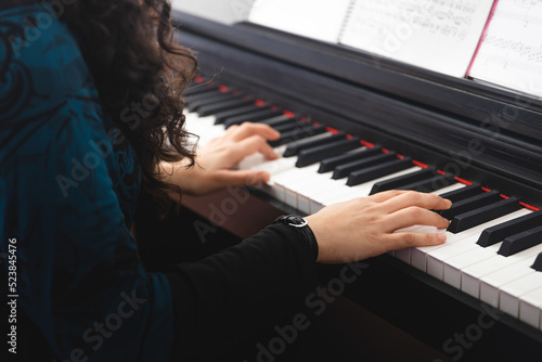 Unrecognizable woman's hands playing piano by reading sheet music. Selective focus