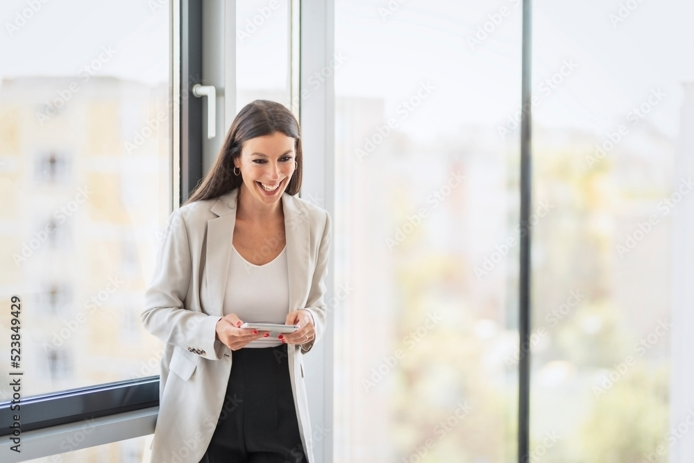 Attractive businesswoman standing at a modern office while using a digital tablet