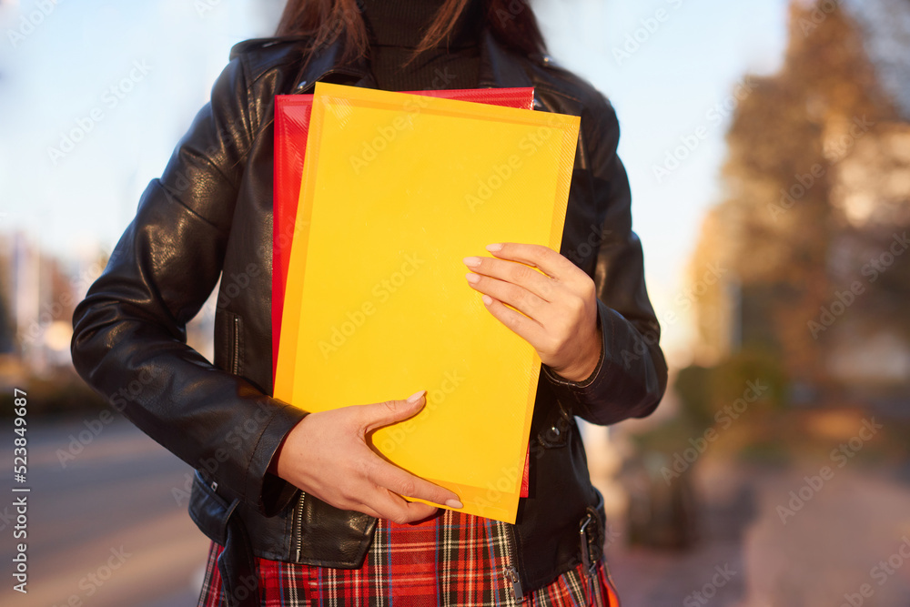 girl student in plaid skirt in university. woman holds yellow and red  folders and notebooks in hands. Learning, education concept Stock Photo |  Adobe Stock