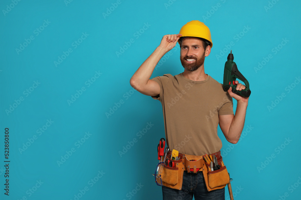 Professional builder in hard hat with tool belt and power drill on light blue background, space for text Professional builder in hard hat with tool belt and power drill on light blue background, space for text