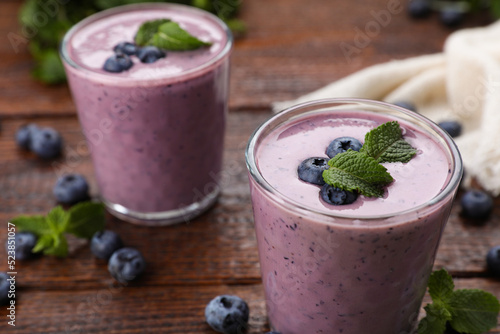 Glasses of blueberry smoothie with mint on wooden table, closeup