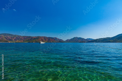 The Boat on the sea surface, feeling of calm and freedom. View from the boat to the blue bay and the green mountains of the island on a sunny day. Travel - image. © Mikhail
