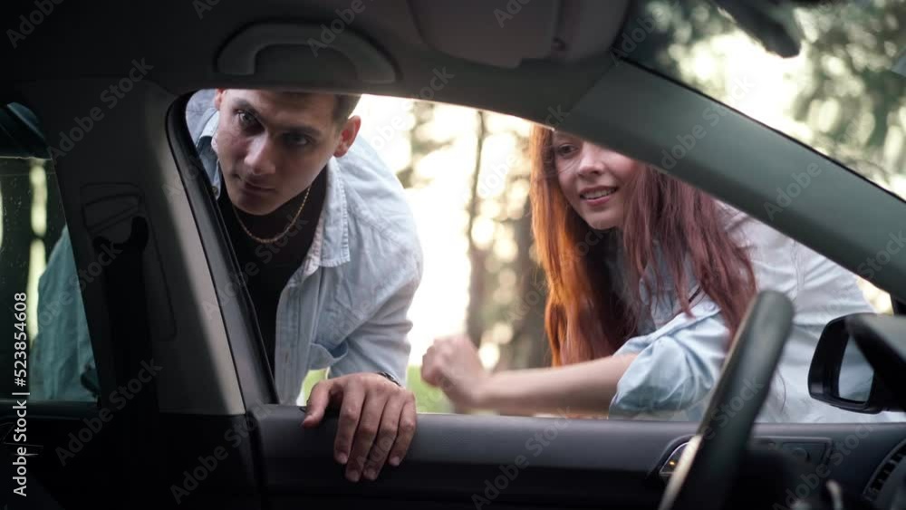 Shooting from car of positive young couple talking looking inside. Smiling Caucasian man and woman in forest at sunset discussing travel plan. Happiness and tourism concept Shooting from car of positive young couple talking looking inside. Smiling Caucasian man and woman in forest at sunset discussing travel plan. Happiness and tourism concept