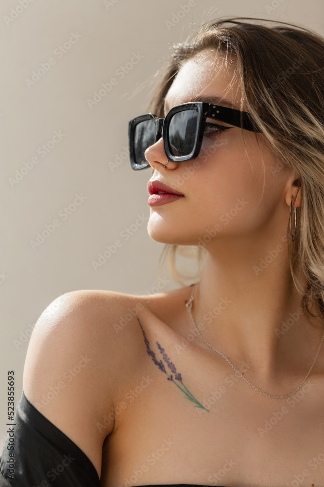 Women's sensual portrait of a beautiful urban fashionable model girl with clean skin with cool hipster sunglasses outside on a sunny day near a wall. Beauty and fashion