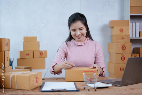 Young owner business woman received orders clients and writing on the products in parcel cardboard box packaging.