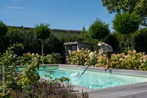 Mann mit Strohhut reinigt an einen Sommertag den Pool mit dem Kescher.