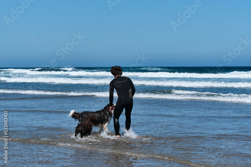 Young surfer boy playing with his border collie dog by the sea