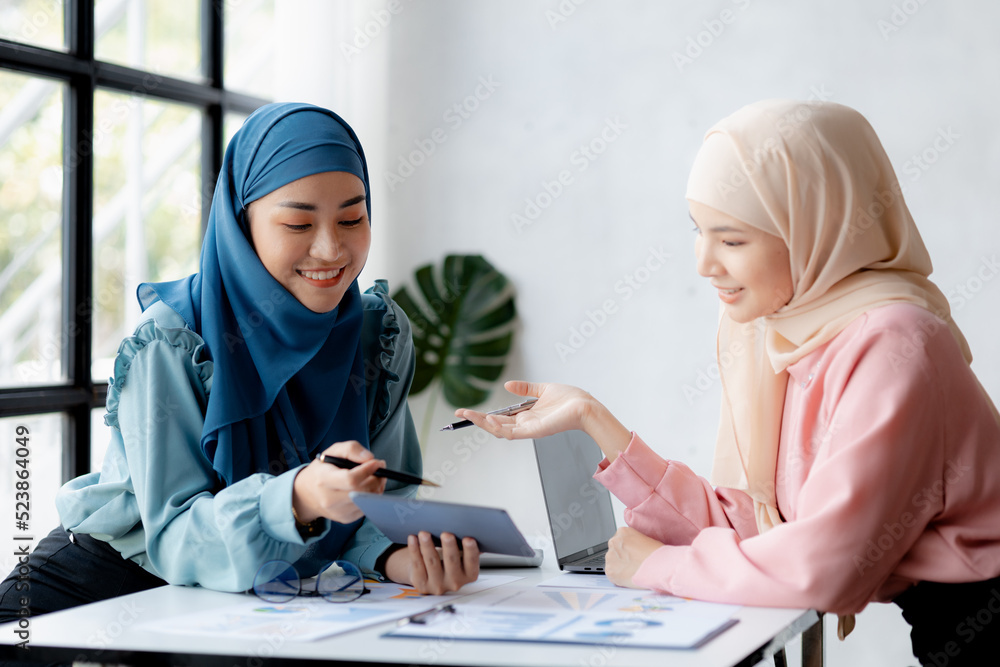Two hijab-clad Asian women are brainstorming together in a conference room for a startup, run by a young, talented woman. The management concept runs the company of female leaders to grow the company. Two hijab-clad Asian women are brainstorming together in a conference room for a startup, run by a young, talented woman. The management concept runs the company of female leaders to grow the company.
