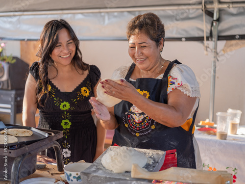 Indigenous mother and daughter smiling while hand pressing tortillas made from masa