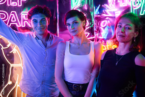 Image of two beautiful women and one man in an amusement park in a room with neon light. Entertainment concept. photo