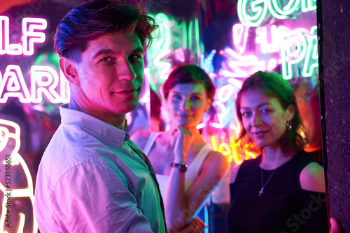 Image of two beautiful women and one man in an amusement park in a room with neon light. Entertainment concept.