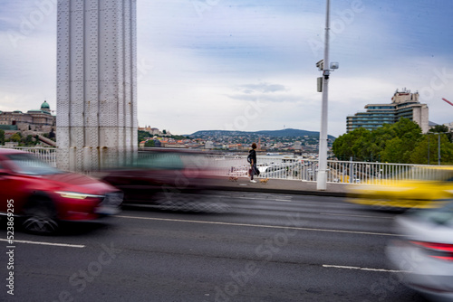Person walks across Erzsébet híd with their dog as cars race past on summers day, Budapest, Hungary 