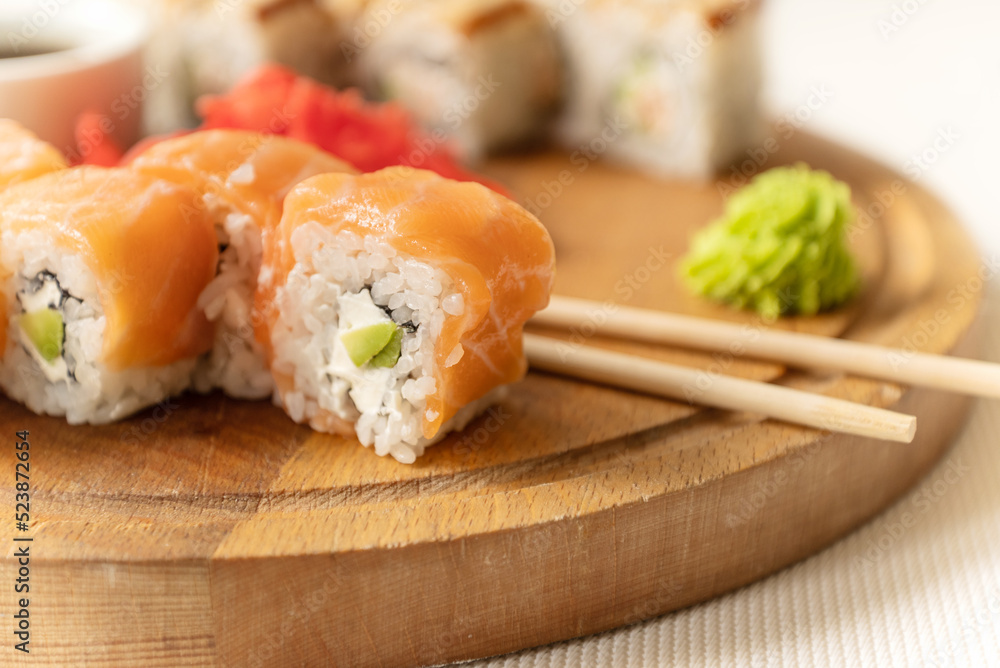 Pieces of fresh salmon philadelphia sushi roll served with wasabi cream and chopstick on wooden board and ready to eat Pieces of fresh salmon philadelphia sushi roll served with wasabi cream and chopstick on wooden board and ready to eat