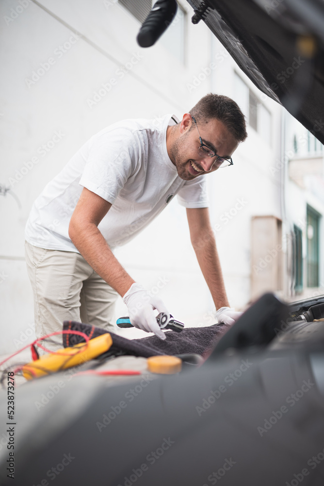 Mecánico joven arreglando un coche felizmente. Joven mecánico feliz con su trabajo.
