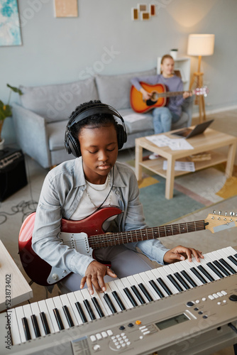 Vertical portrait of black young woman playing music at home and wearing headphones