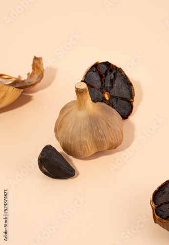 Black garlic bulbs and cloves lie on a beige table. A conceptual composition of fermented food with a hard shadow. Healthy nutrition, vegetarian food, self-care