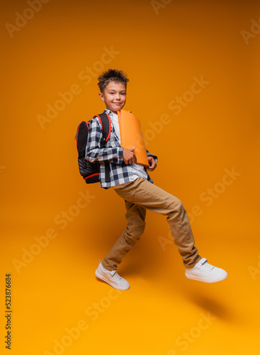 Side view of a happy schoolboy, smiling and carrying a folder, going to school on a yellow background. portrait of a schoolboy.