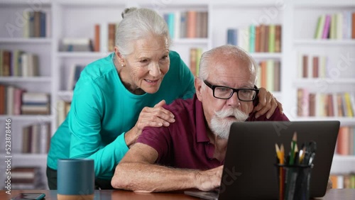 Happy senior elderly couple man and woman in home office using laptop.