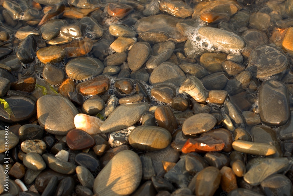 A pure transparent sea wave rolls over the rocky pebble shore, the concept of rest and travel, tranquility, relaxation and reflection on a warm summer day, close-up. A pure transparent sea wave rolls over the rocky pebble shore, the concept of rest and travel, tranquility, relaxation and reflection on a warm summer day, close-up.