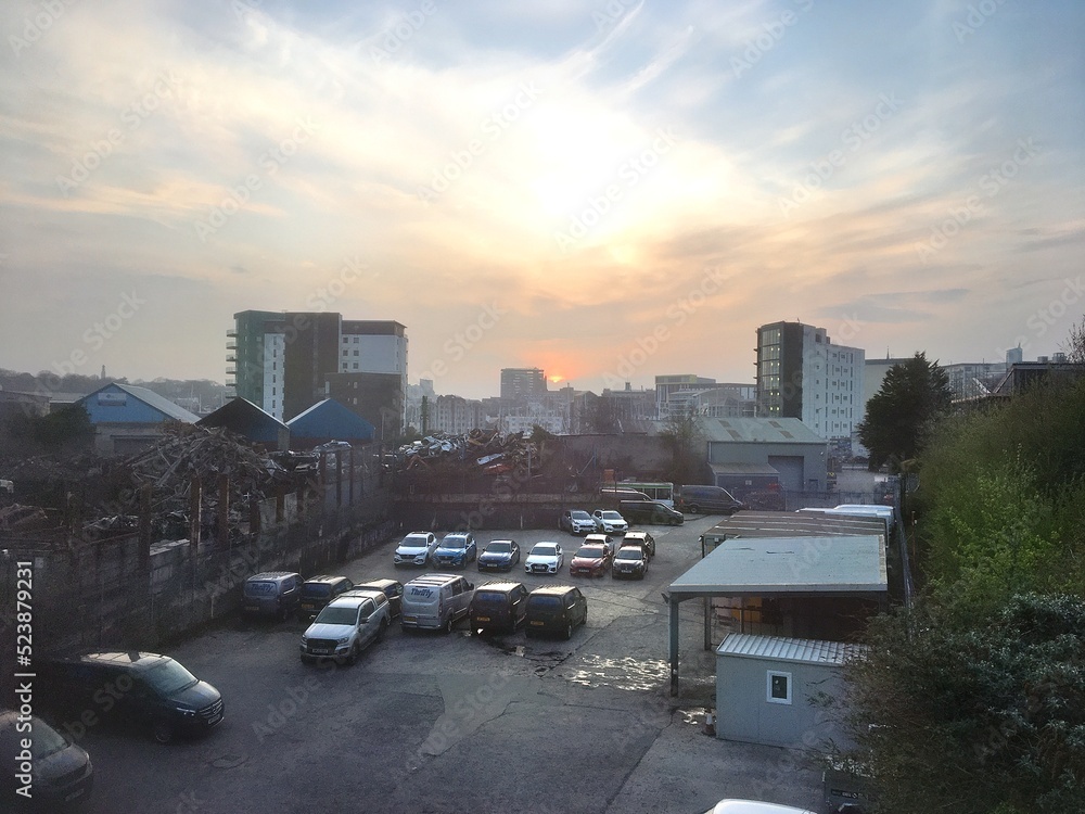 Industrial car park cityscape with city skyline, sunset and hazy sky with rental vans and trucks and other vehicles