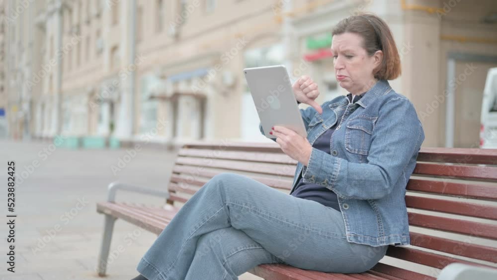 Old Woman Reacting to Loss on Tablet while Sitting Outdoor on Bench Old Woman Reacting to Loss on Tablet while Sitting Outdoor on Bench