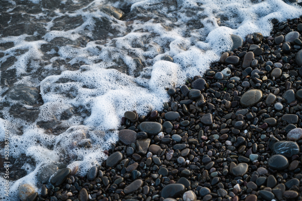 Close-up of small stones on pebbled beach. Sea foam. Close-up of small stones on pebbled beach. Sea foam.