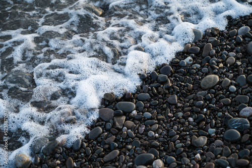 Close-up of small stones on pebbled beach. Sea foam.
