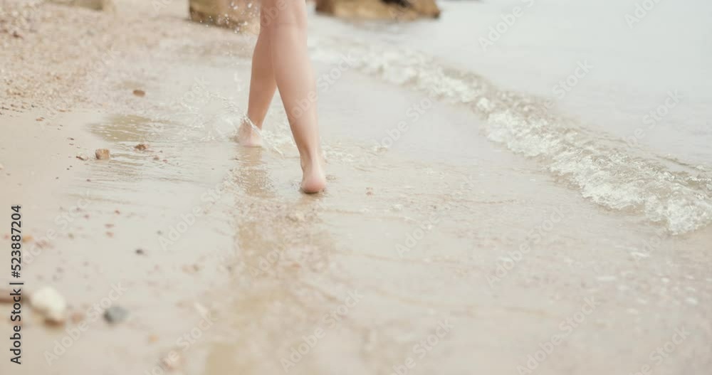 Close-up of an unrecognizable female teenager's legs is walking along the empty sandy sea beach. Close-up of an unrecognizable female teenager's legs is walking along the empty sandy sea beach.