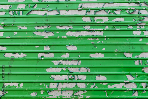 Peeling green paint in messy pattern on corrugated metal surface photo