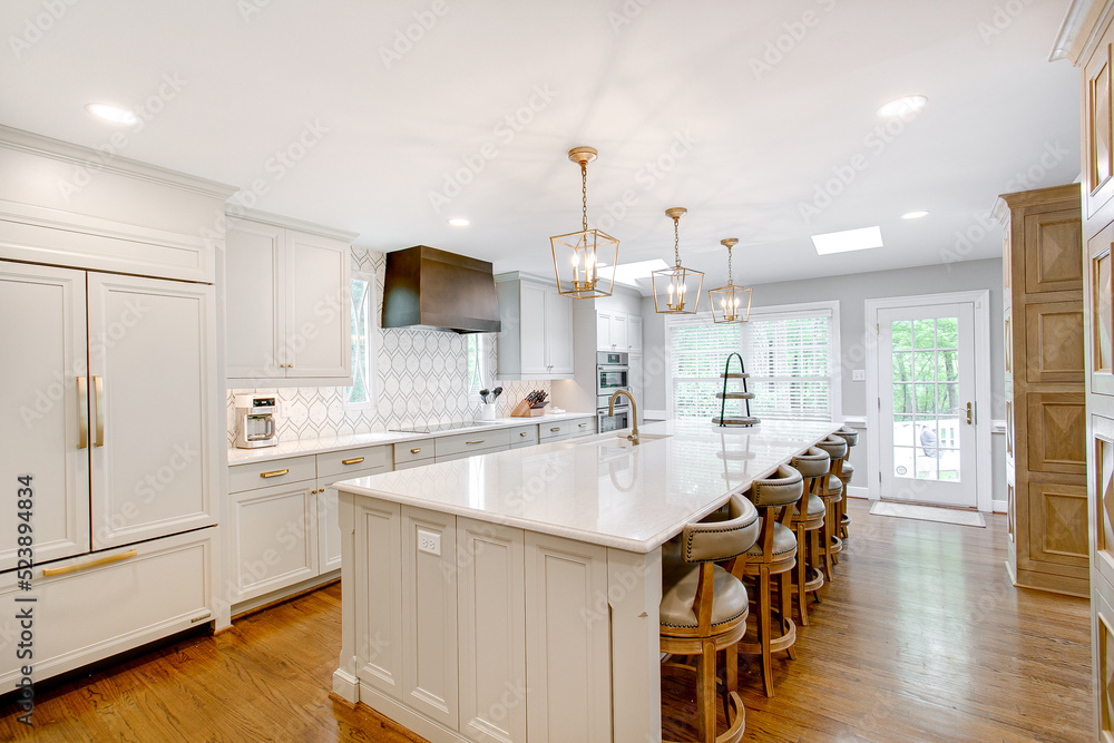 Luxury interior staged kitchen white stone countertops decor stools ceramic tile backsplash modern brass light pendants wood columns