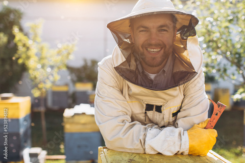 Portrait of a happy male beekeeper working in an apiary near beehives with bees. Collect honey. Beekeeper on apiary. Beekeeping concept.