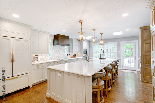 Obraz na płótnie Luxury interior staged kitchen white stone countertops decor stools ceramic tile backsplash modern brass light pendants wood columns w salonie