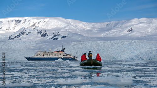 Zodiac inflatable boat navigating among icebergs, away from an expedition cruise ship, in Cierva Cove, Antarctica