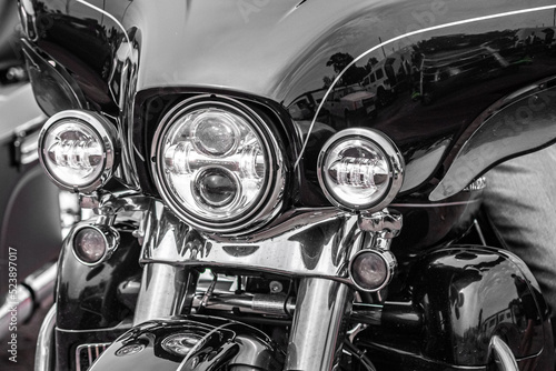 Part of a motorcycle. Chrome details. Three headlights. Biker background. Two-wheeled transport. Front view. Close-up of the front of a motorcycle with three headlights. 