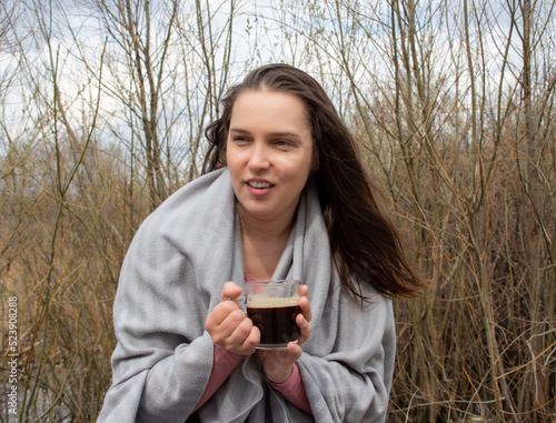 a woman drinks coffee in winter or early spring in nature. woman in plaid with a cup of hot coffee