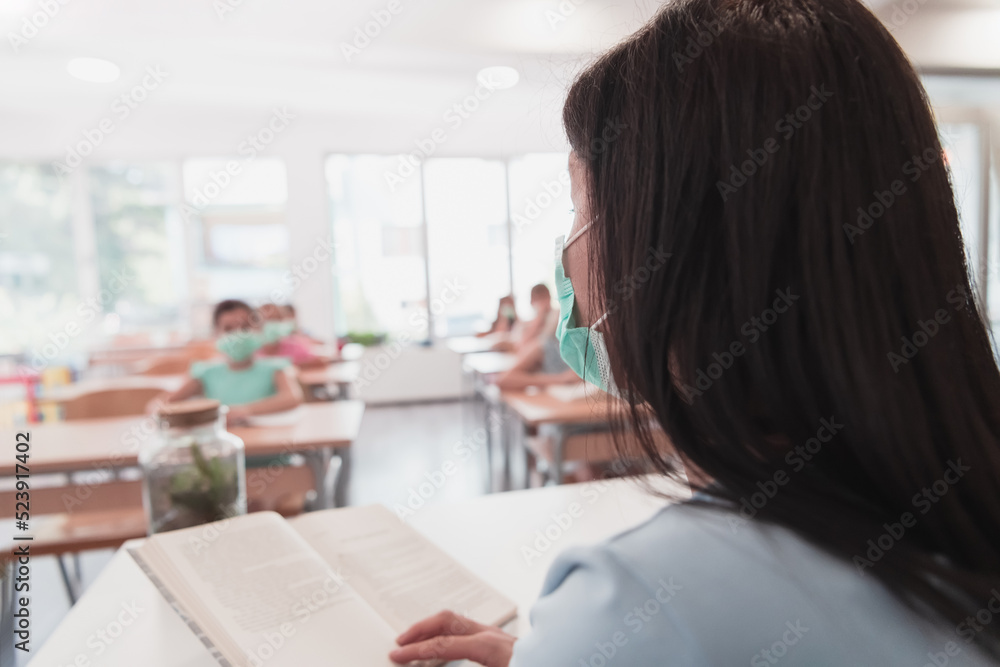 Multiracial group of kids wearing face masks working at class, writing and listening explanations of teacher in classroom Multiracial group of kids wearing face masks working at class, writing and listening explanations of teacher in classroom
