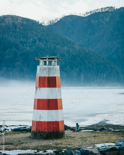 Vertical shot of a red and white lighthouse on the shore against the background of green hills.