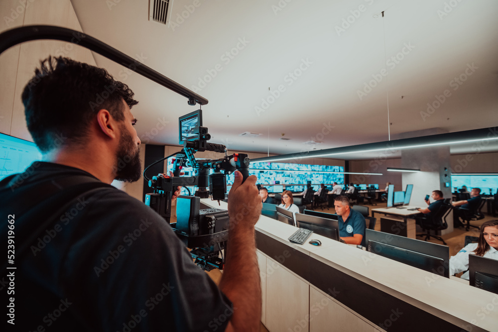 Professional videographer with gimball video slr recording video of Security data center operators while working in a CCTV monitoring room looking on multiple monitors Team working on the System Con