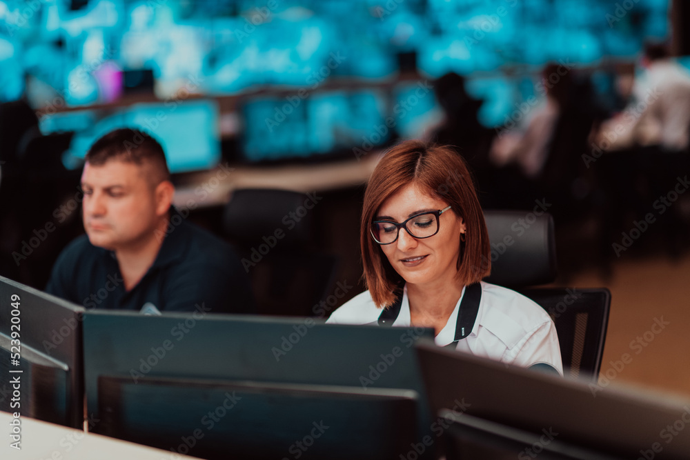 Female security operator working in a data system control room offices Technical Operator Working at workstation with multiple displays, security guard working on multiple monitors Female security operator working in a data system control room offices Technical Operator Working at workstation with multiple displays, security guard working on multiple monitors