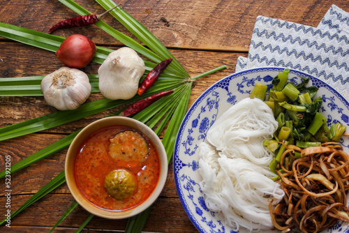 Thai rice noodle with peanut sauce served in a white plate on a wooden table and decorated with leaves.