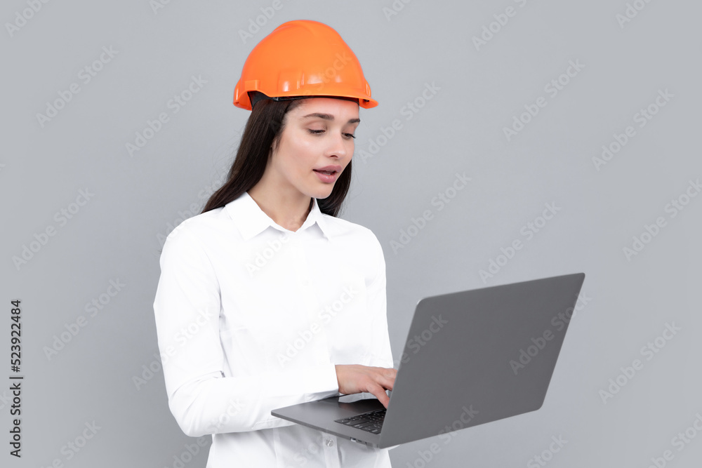 Young woman in helmet hold laptop computer on gray background. Architect businesswoman in helmet thinking, young caucasian female in work as constructor engineer. Young woman in helmet hold laptop computer on gray background. Architect businesswoman in helmet thinking, young caucasian female in work as constructor engineer.