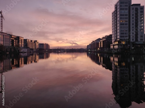 Photography Buildings reflecting on a canal at sunset with industrial smoke in the distance